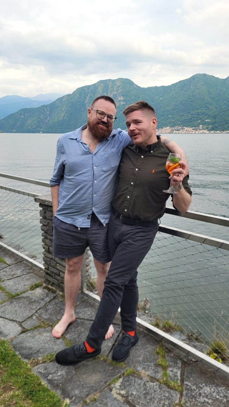 Me and my husband, arms around each other on a stone terrace above Lake Como, mountains and water behind us