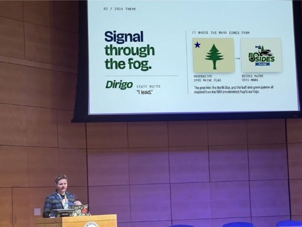 A conference slide reading 'Signal through the fog. Dirigo, I lead.' showing how a modernized 1901 Maine flag inspired the BSides Maine 2026 logo