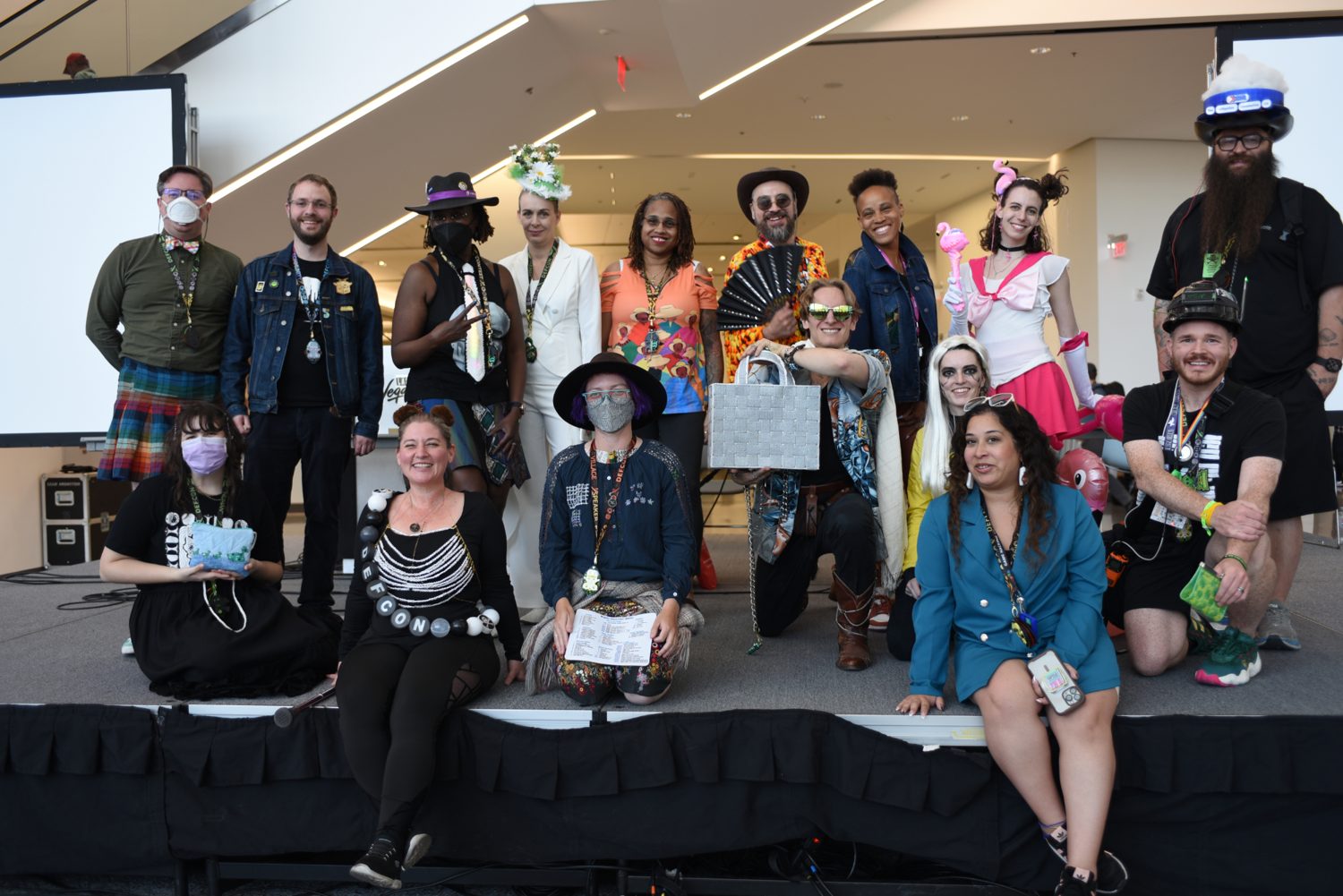 About fifteen DEF CON Hacker Runway participants posing together on a stage in elaborate, creative hacker outfits