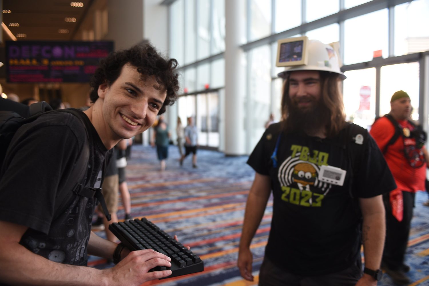 A DEF CON attendee wearing a hard hat with a small text display while another person types a question to it