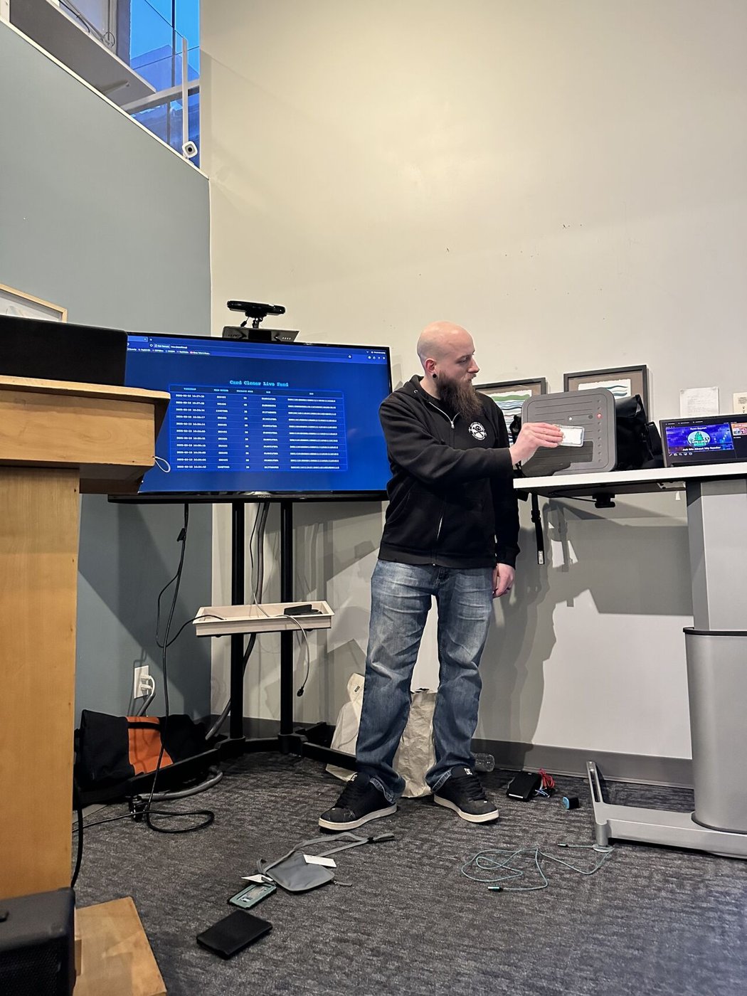 A presenter at DC207 holding an access badge to a reader while the screen behind him shows a live 'Card Cloner Live Feed' of captured card data