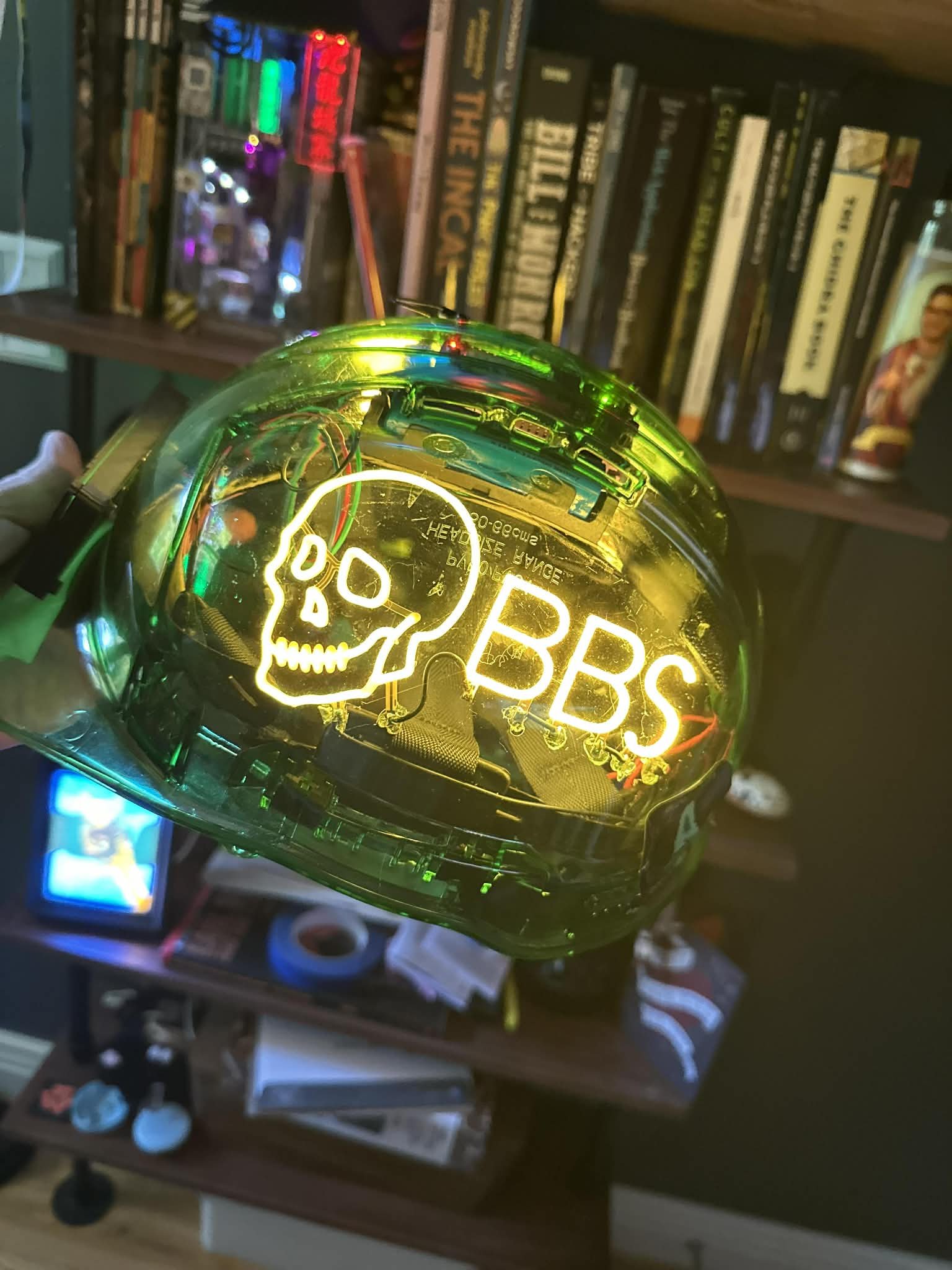 A translucent green hard hat held up in a dim room, a glowing skull-and-BBS logo in EL wire across the shell, with the Pi, wiring and battery visible through the plastic.